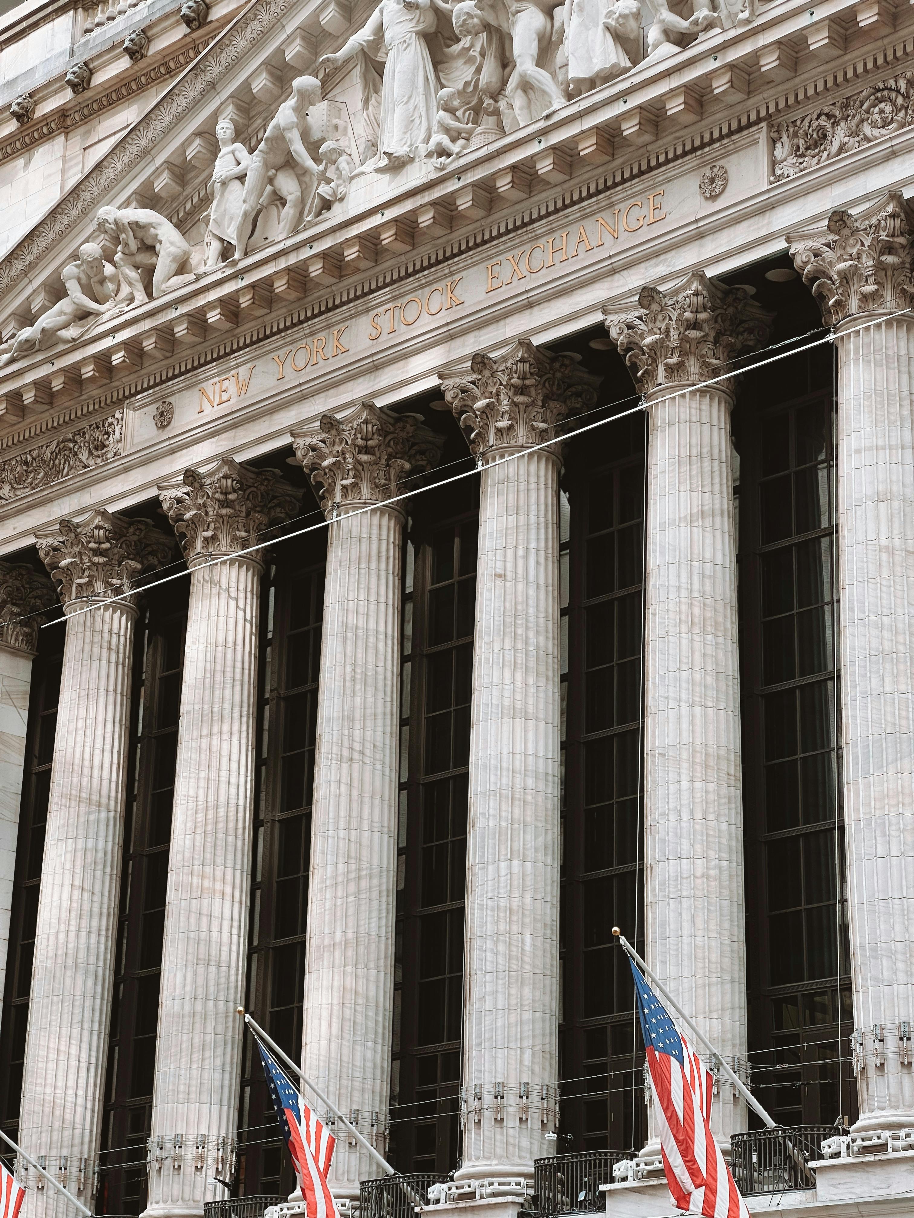 New York Stock Exchange facade with American flags and neoclassical columns on a clear day