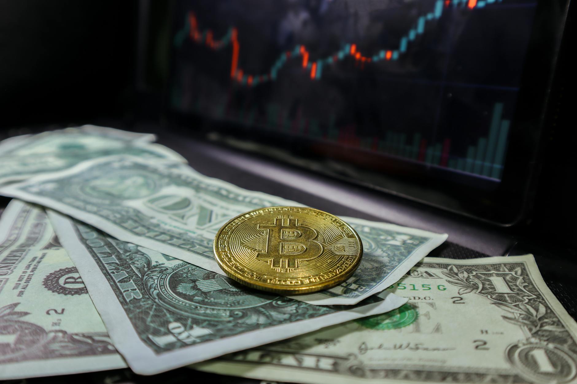 Bitcoin coin on US dollar bills with a stock market chart in the background, representing the intersection of cryptocurrency and traditional banking